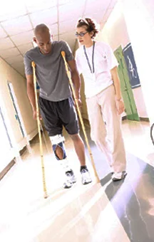 An injured man on crutches walking a hallway beside a nurse